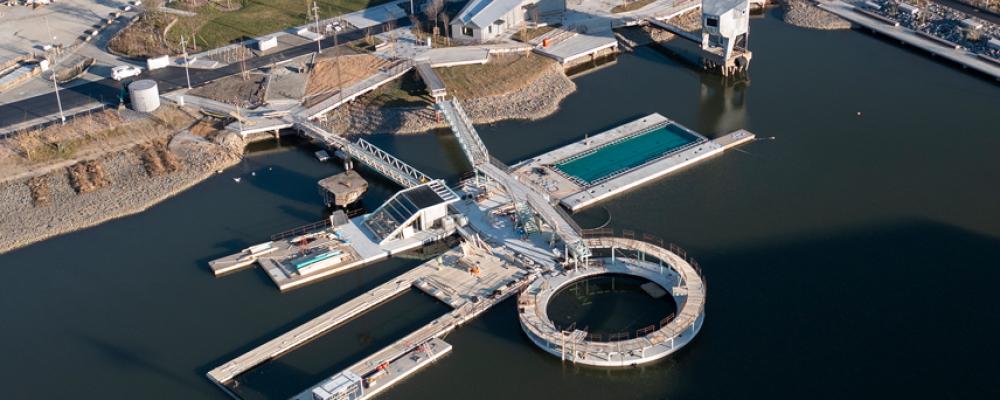 Hamnbadet i Jubileumsparken, Frihamnen 7 i Göteborg. Två naturvattenpooler och en sötvattenpool med naturlig rening, flytande ytan totalt ca 1008 m² och bassängerna sammanlagt ca 580 m². Befintliga pontoner och bassäng har återanvänts. Pontonerna är exceptionellt stora, gjutna och levererade på sänkbar pråm. Speciellt för hamnbadet är också diamantformade pontonen i mitten och den runda pontonen med hopptorn utanpå. Foto: