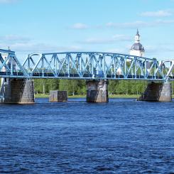 Järnvägsbron över Torne-älv. En bro mellan svenska Haparanda och den östra delen av den finska staden Torneå. Ursprungligen kunde mittspannet vändas för att låta höga skepp passera. Bakom ryttarna kyrkan i Alatornio. Foto: Wikipedia, kredit: Bobo11